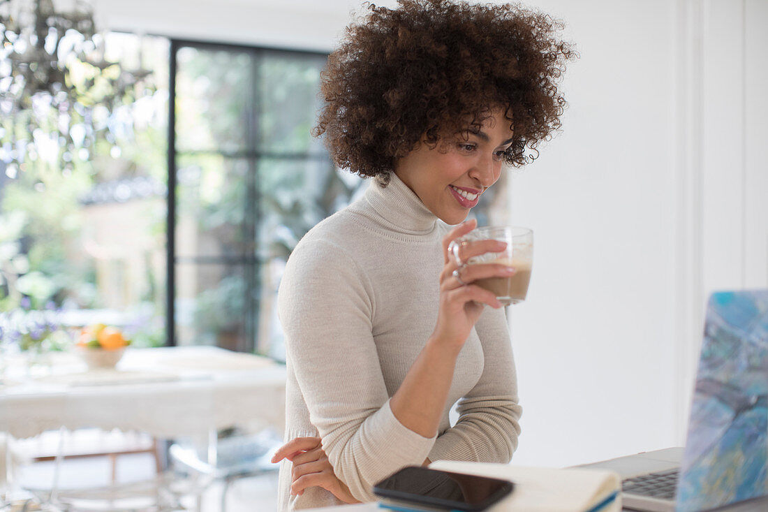 Young female freelancer drinking coffee at laptop