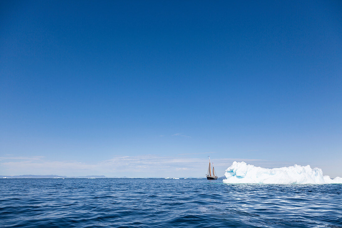 Ship sailing behind iceberg on blue