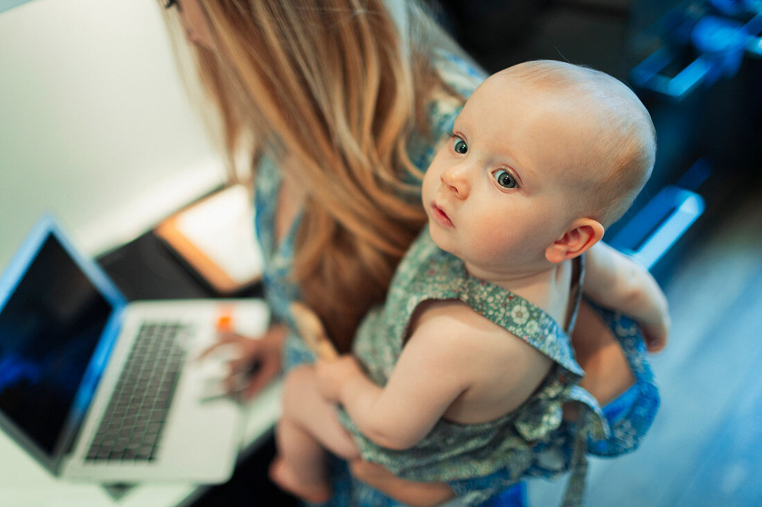 Mother working at laptop and holding cute baby daughter