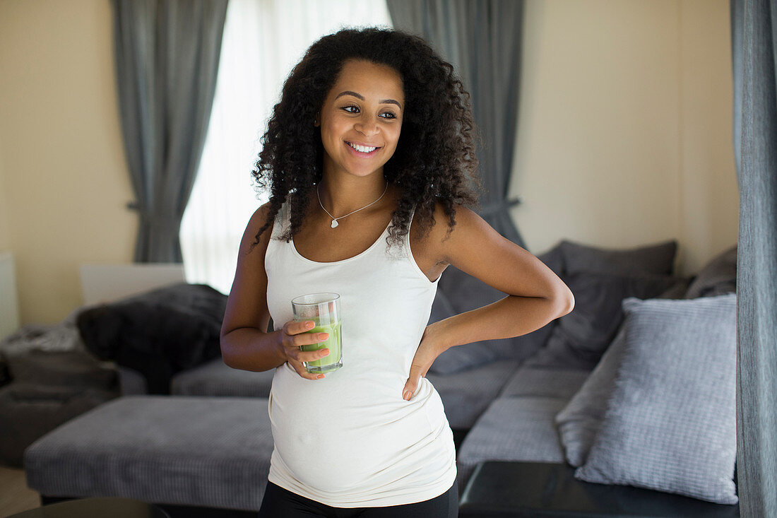 Pregnant woman drinking green smoothie in living room