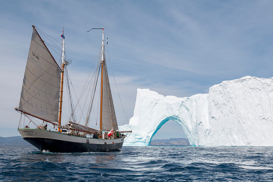 Ship sailing by iceberg arch on blue