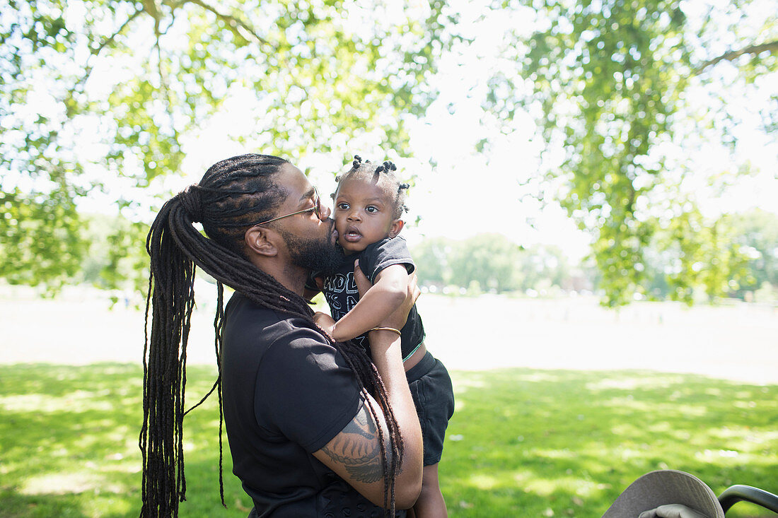Father with long braids kissing toddler son in park