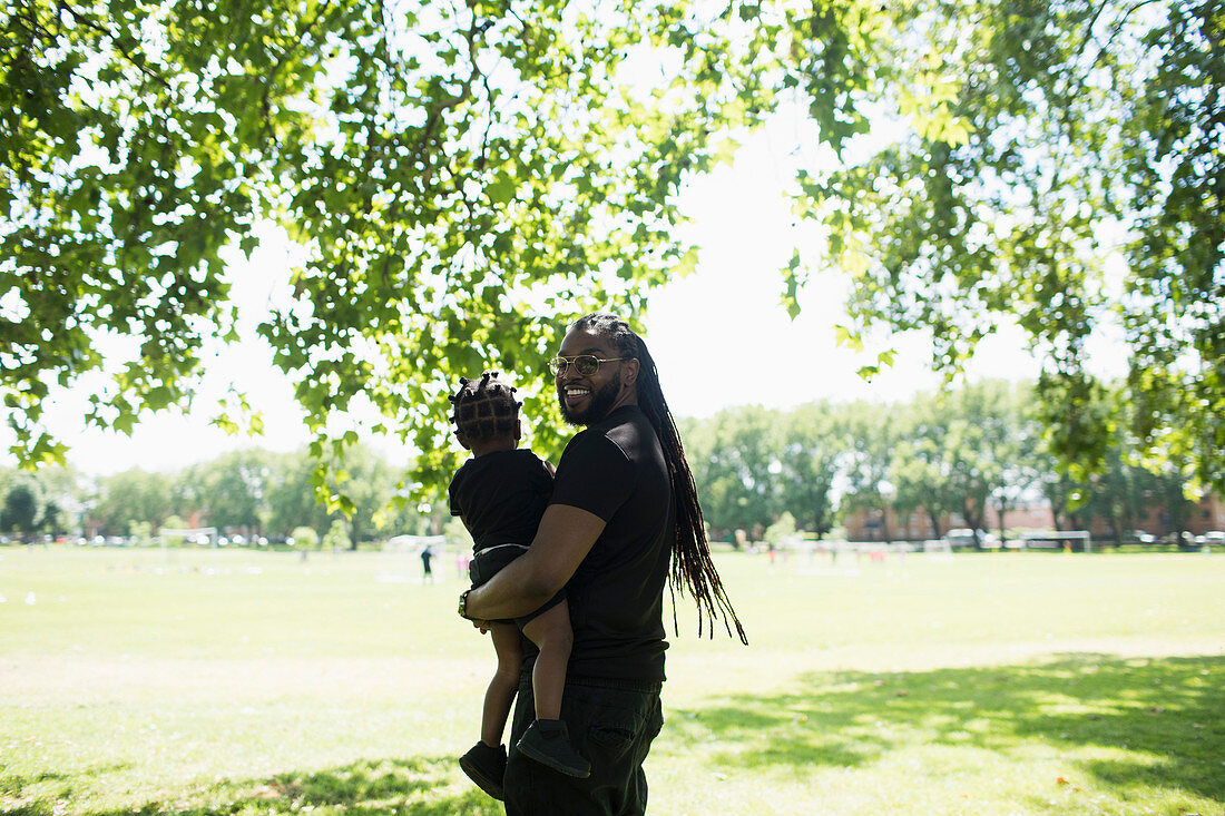 Father with long braids carrying son in park