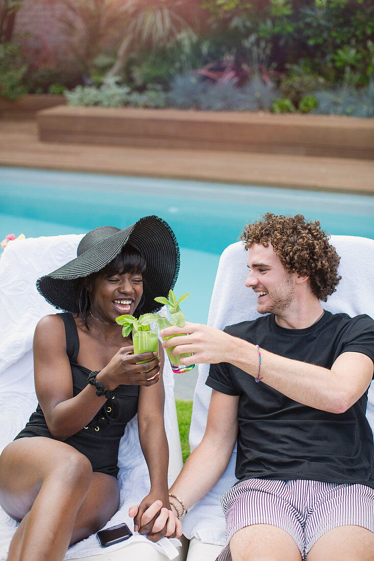Happy multiethnic couple drinking cocktails at poolside