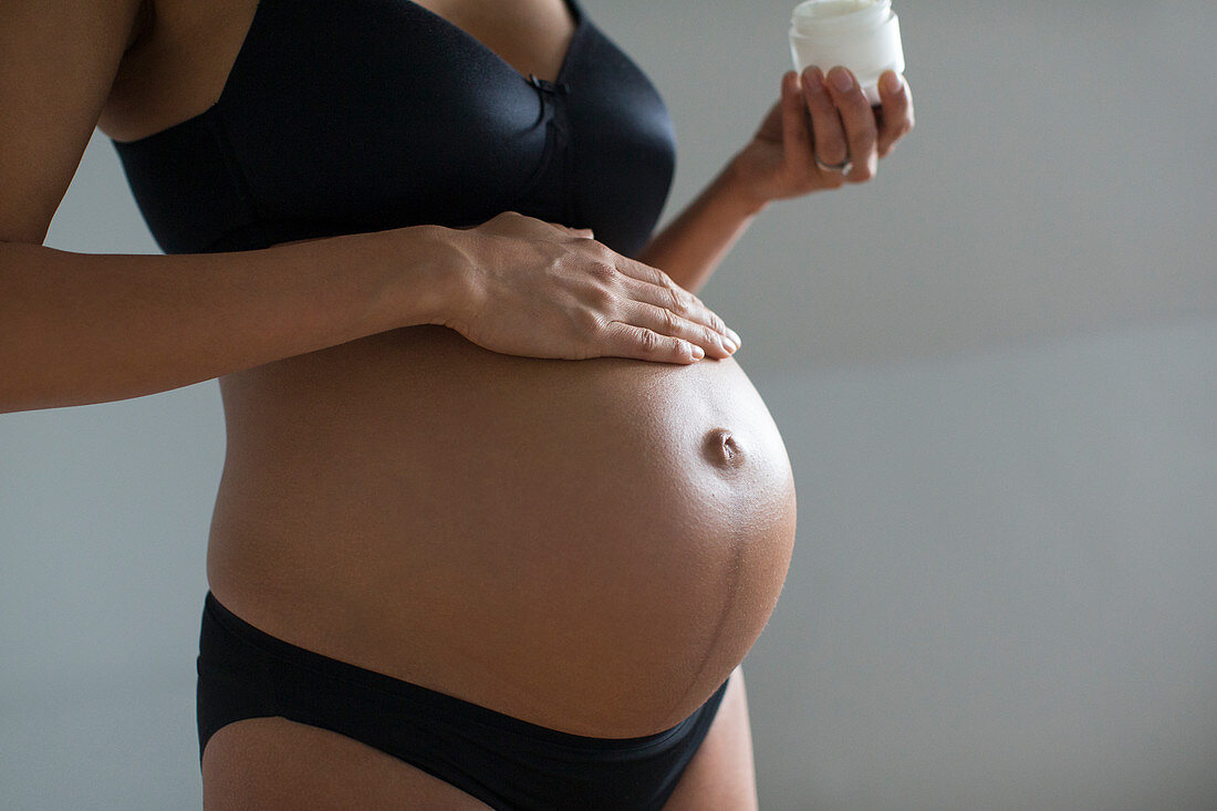 Close up pregnant woman applying moisturizer to stomach