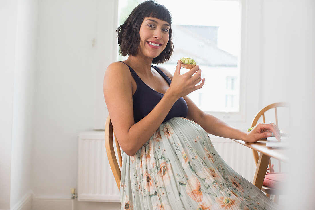 Portrait happy pregnant woman eating avocado toast