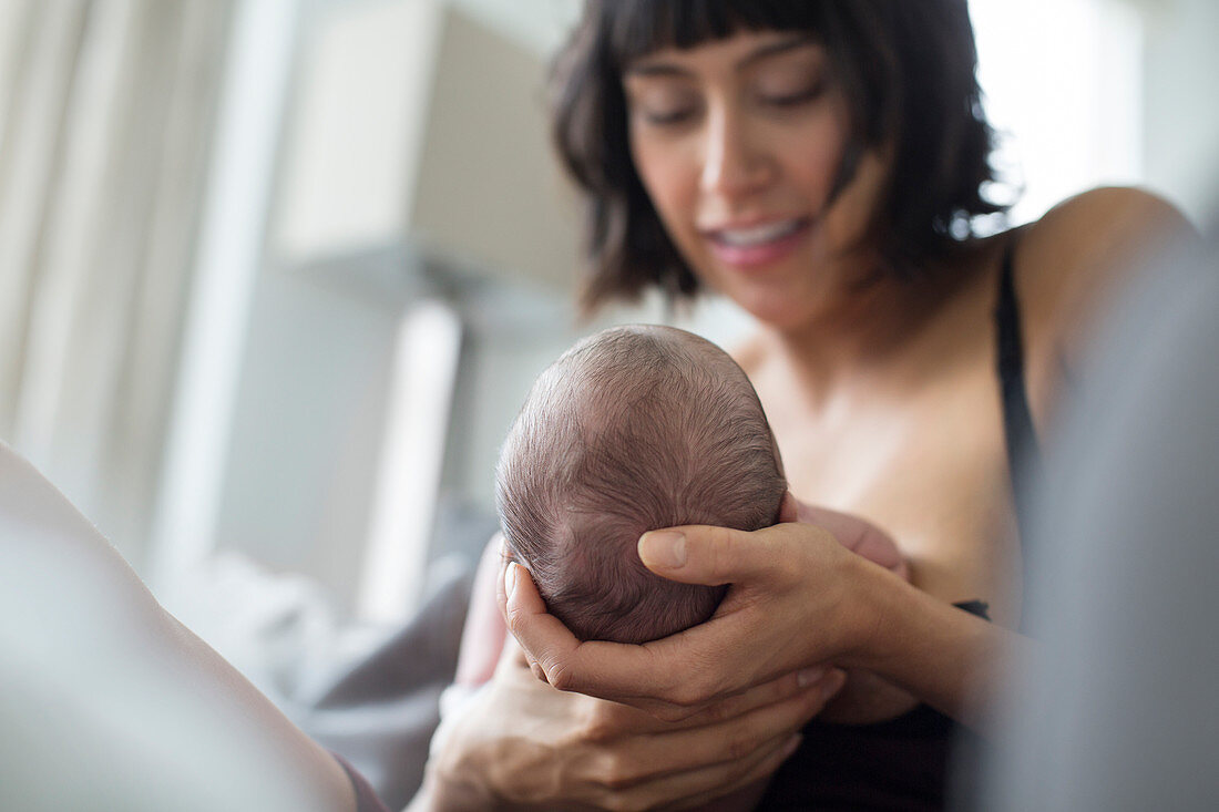 Mother cradling and breastfeeding newborn baby son