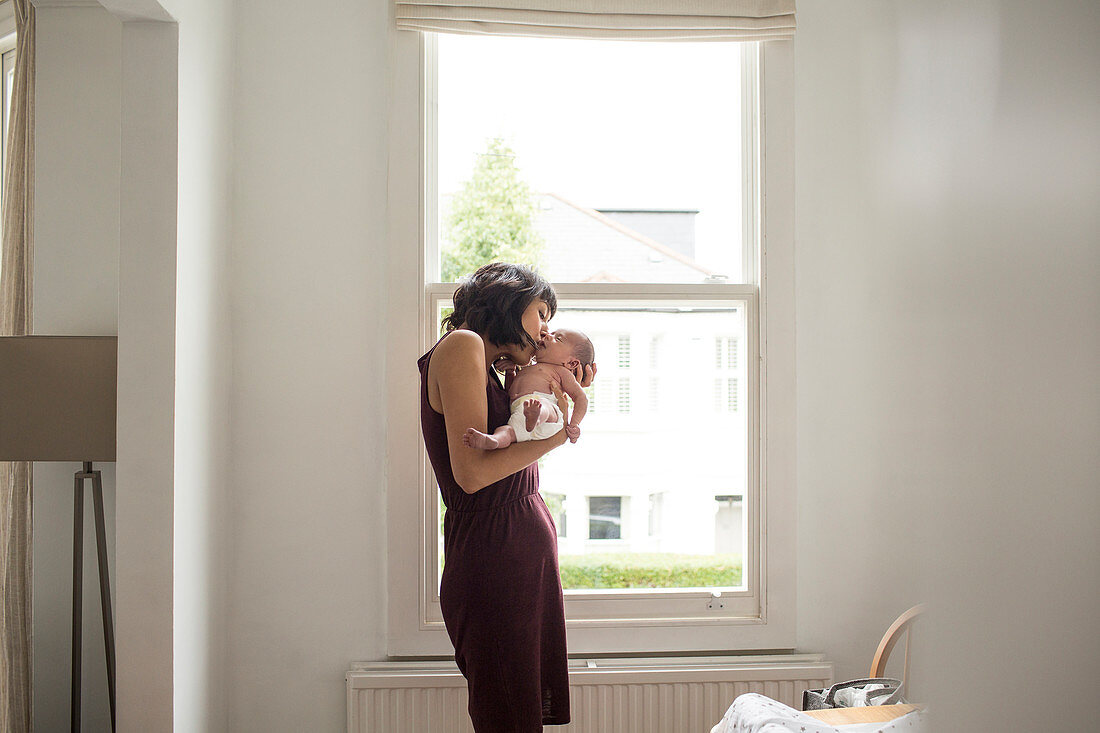 Mother kissing newborn baby son in window