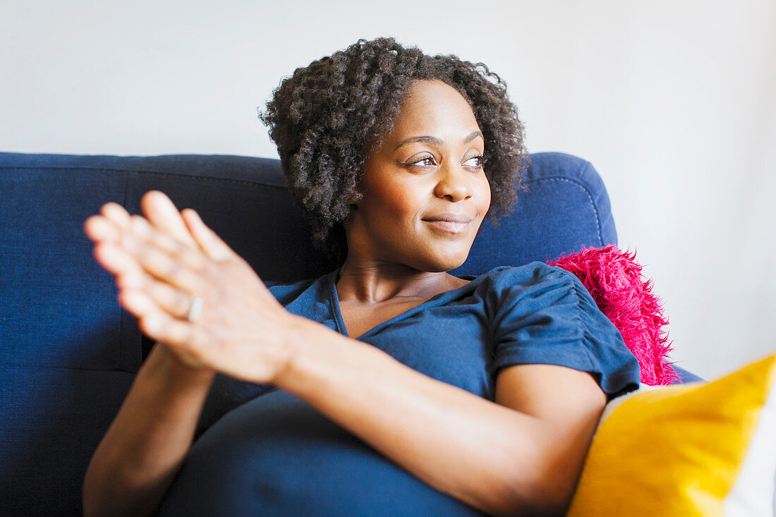 Happy pregnant woman rubbing hands together on sofa