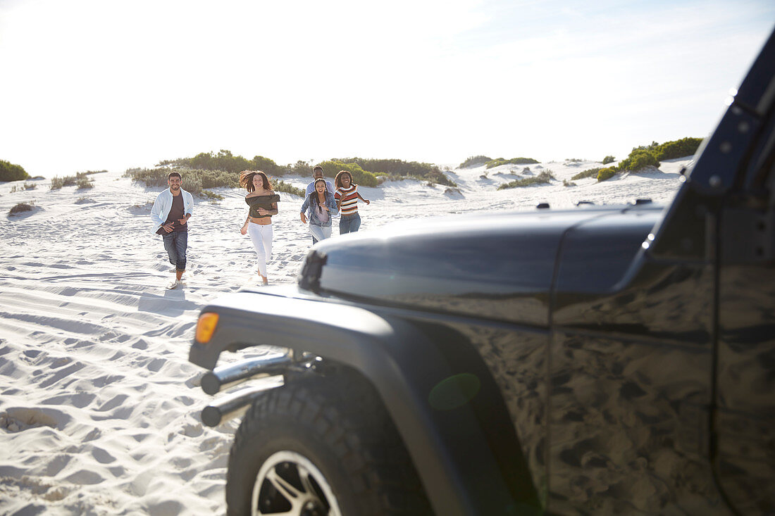Young friends running on sunny beach toward jeep