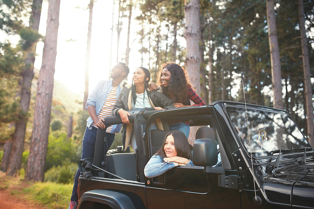 Young friends in jeep looking up at trees in woods