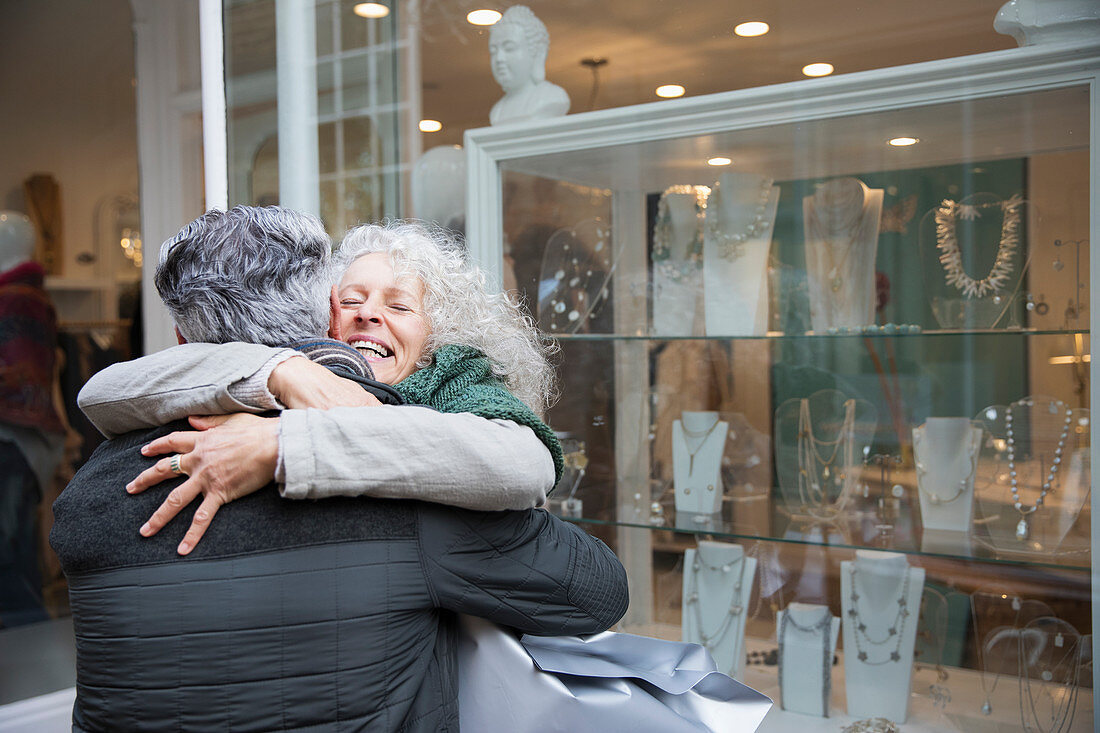 Senior couple hugging, window shopping at jewelry storefront