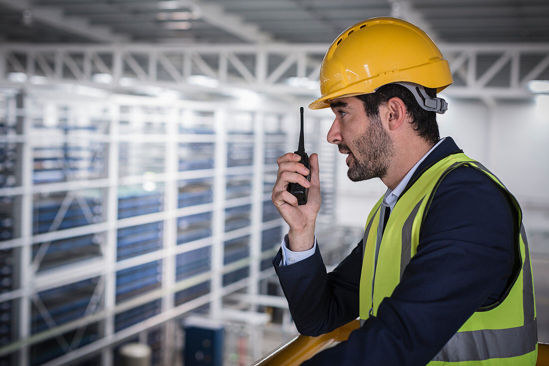 Male supervisor using walkie-talkie on platform in factory
