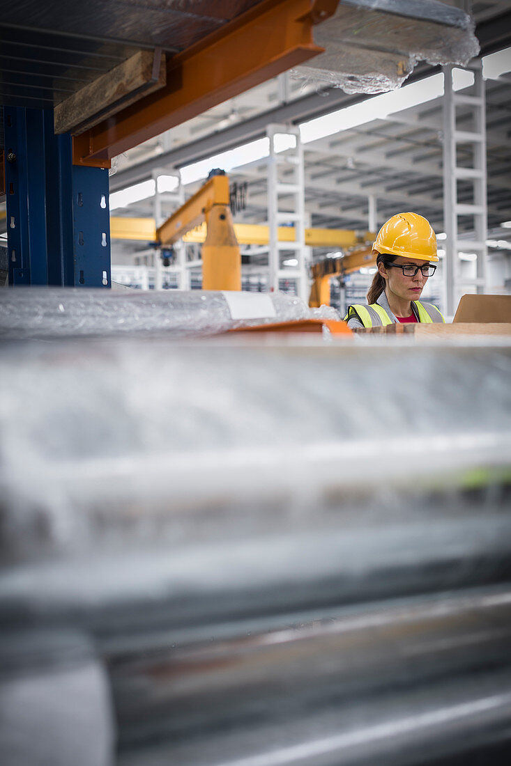 Focused female worker using laptop in steel factory
