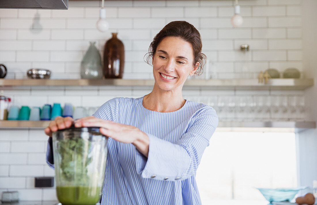 Smiling woman making healthy green smoothie in blender