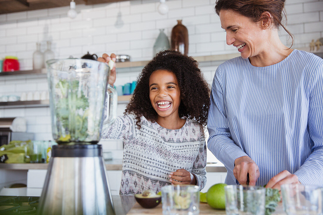 Mother and daughter making healthy green smoothie in kitchen