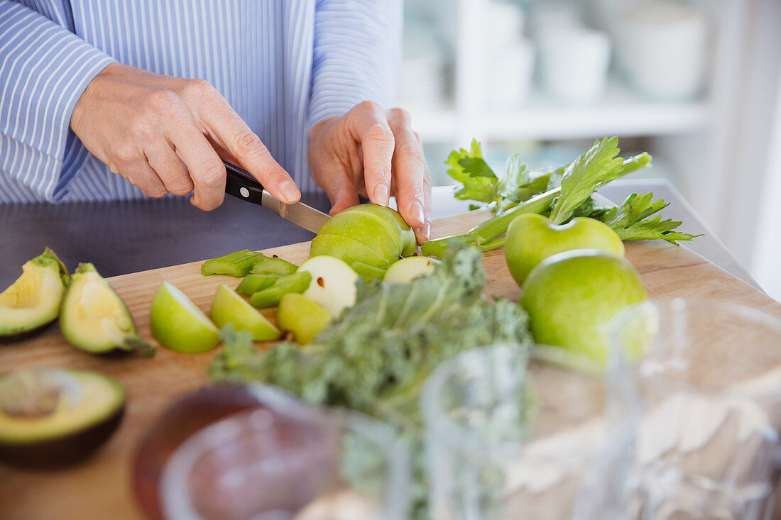 Woman cutting green apples and produce on cutting board