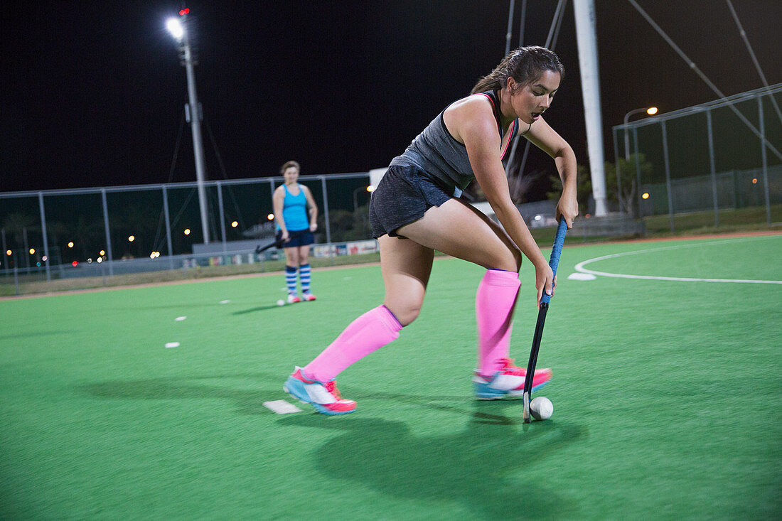 Young female field hockey player playing on field at night