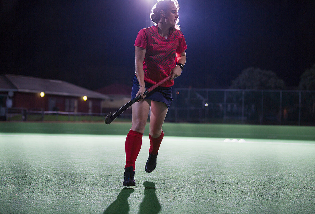 Female hockey player running with hockey stick on field