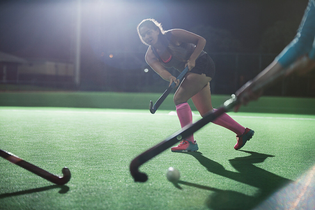 Female hockey running with hockey stick on field at night