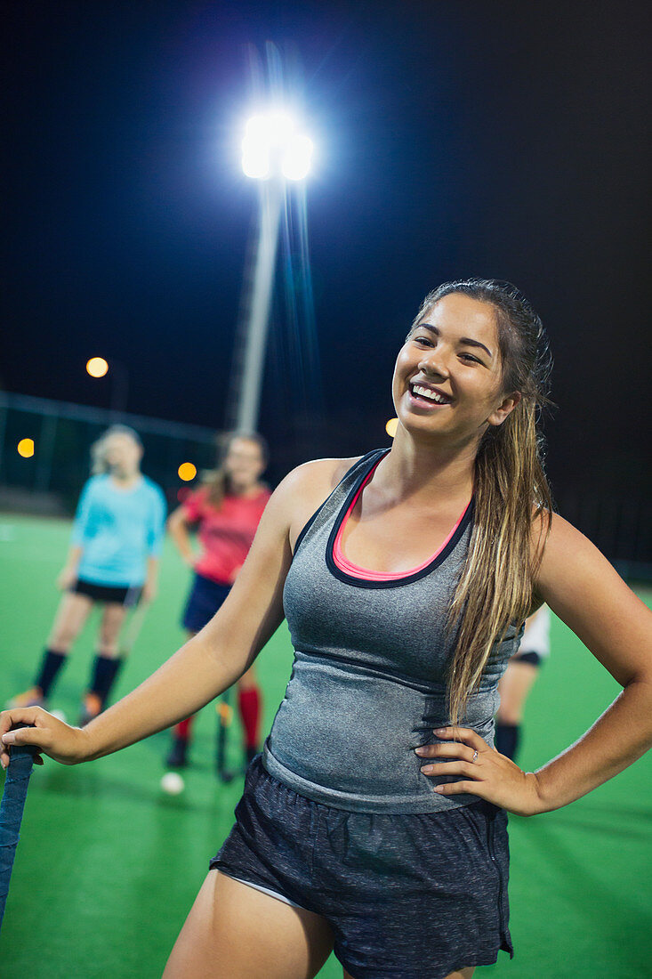 Smiling young female field hockey player on field at night