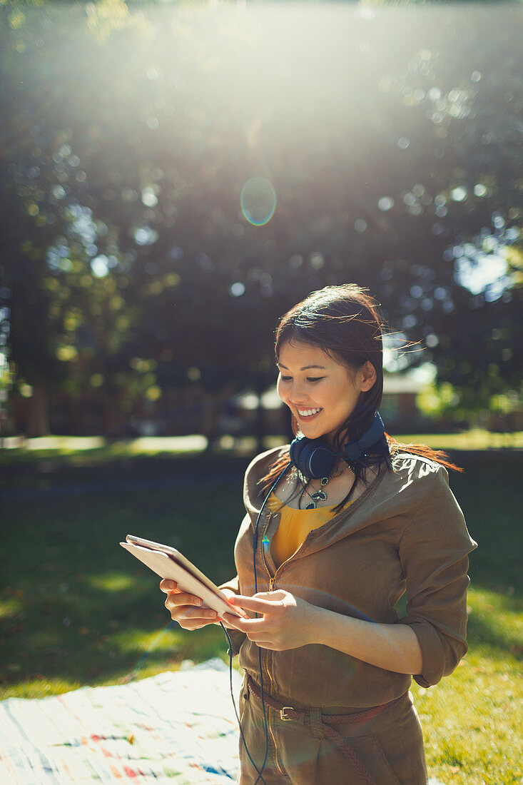 Woman with headphones using tablet in sunny park