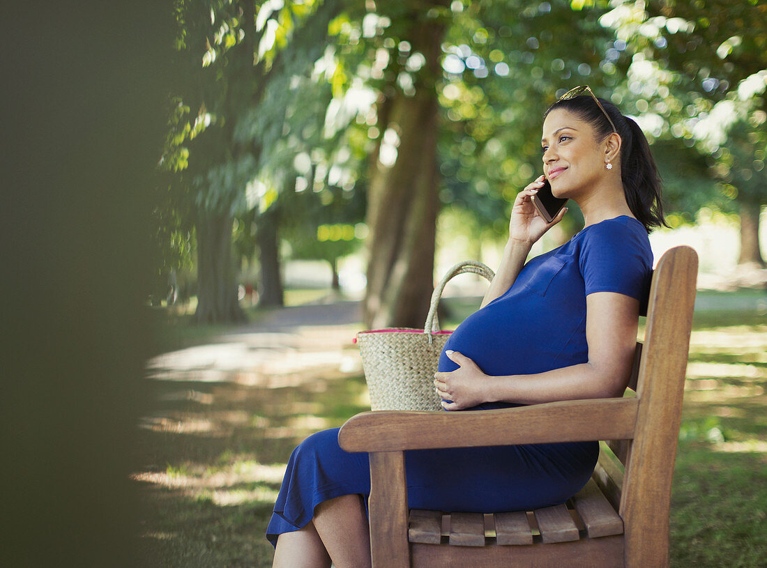 Pregnant woman talking on cell phone on park bench
