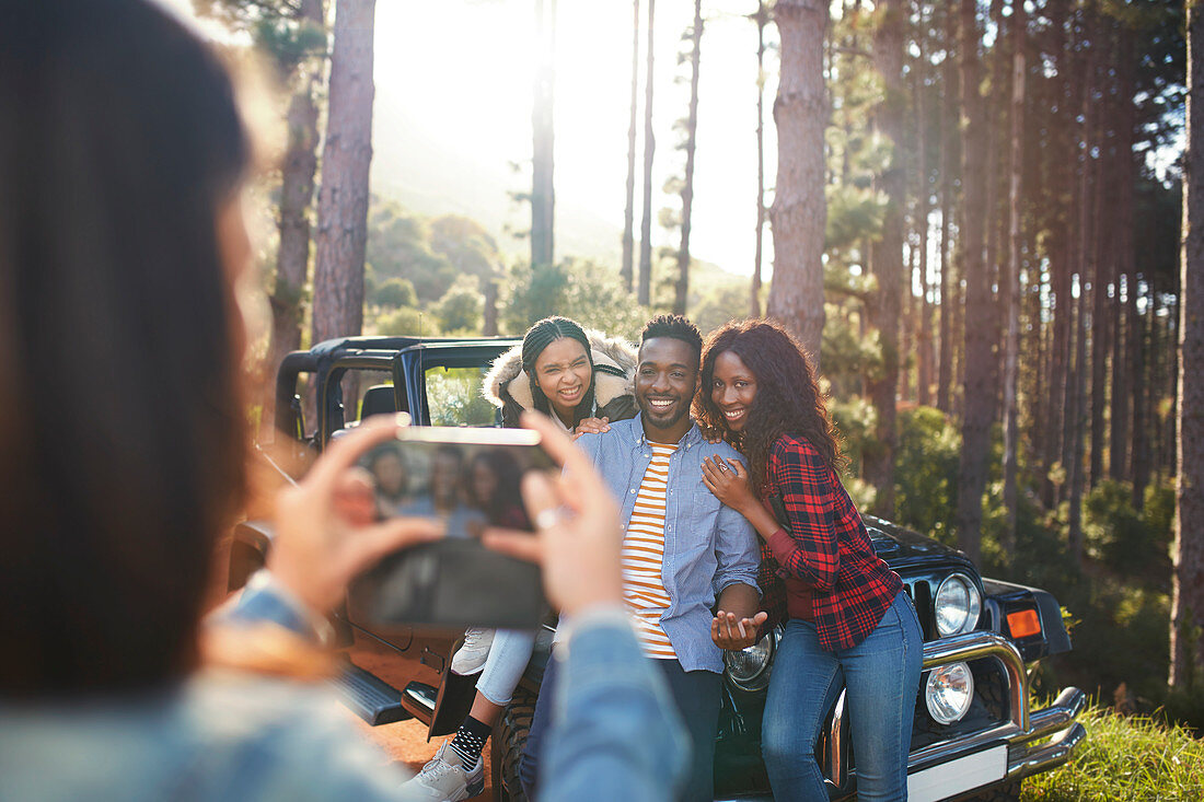 Young woman photographing friends at jeep in woods