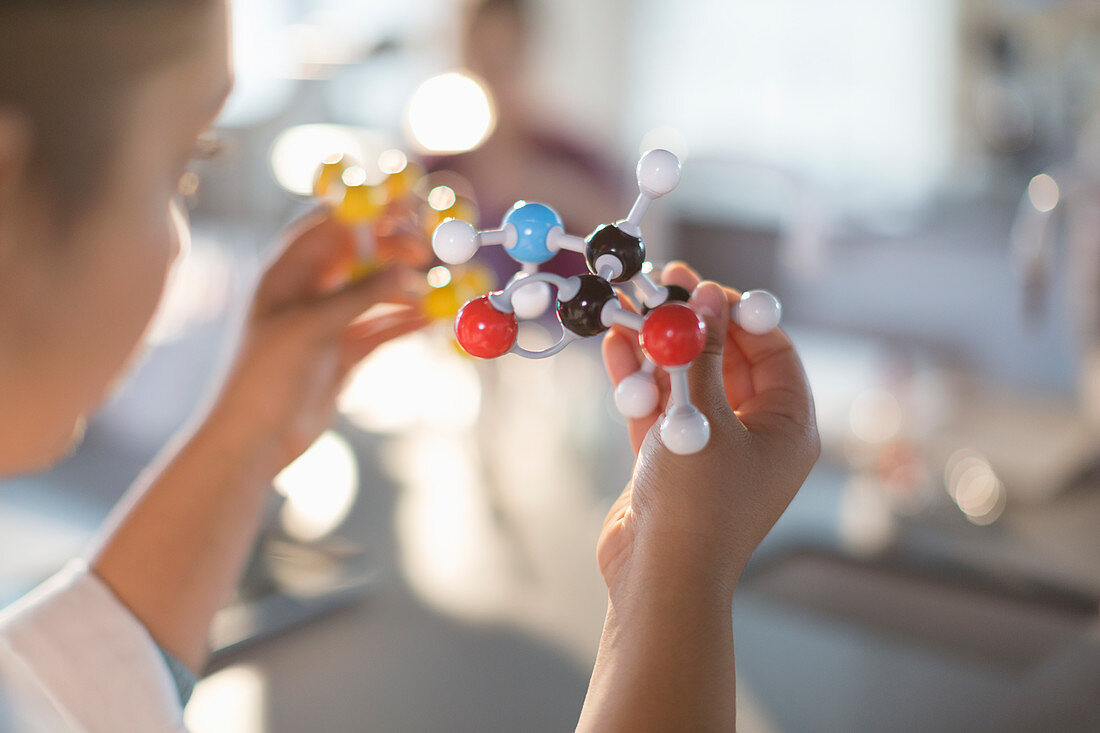 Curious girl student holding molecule model in classroom