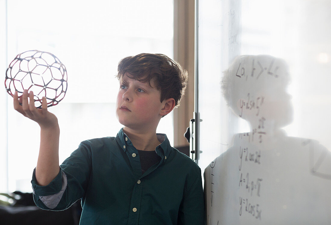 Serious boy student holding molecular structure in classroom