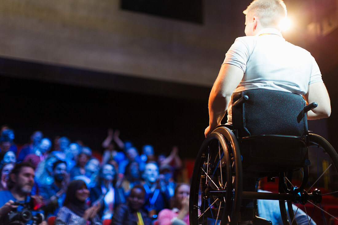 Audience clapping for female speaker in wheelchair on stage