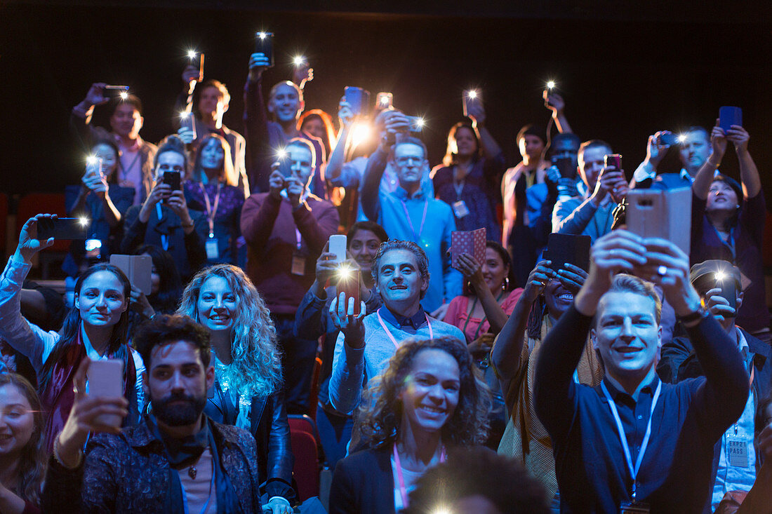 Audience with smart phone flashlights in dark auditorium