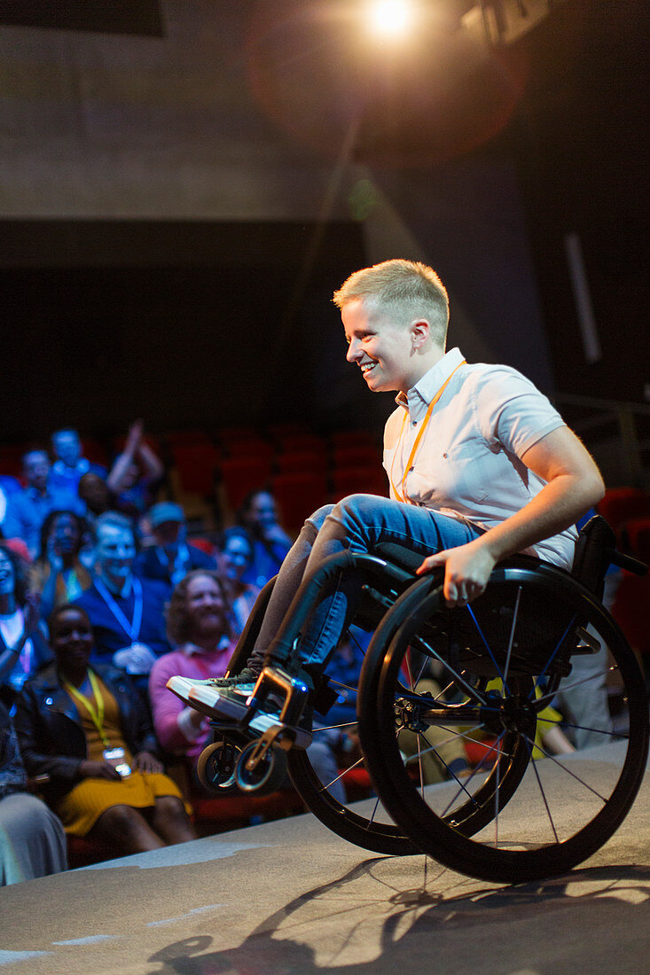 Female speaker doing a wheelie in wheelchair on stage