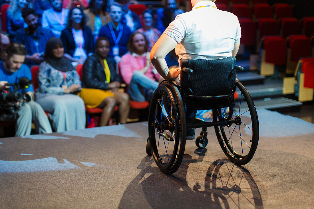 Audience watching female speaker in wheelchair on stage