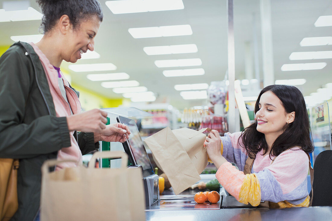 Female cashier helping customer bag groceries at supermarket