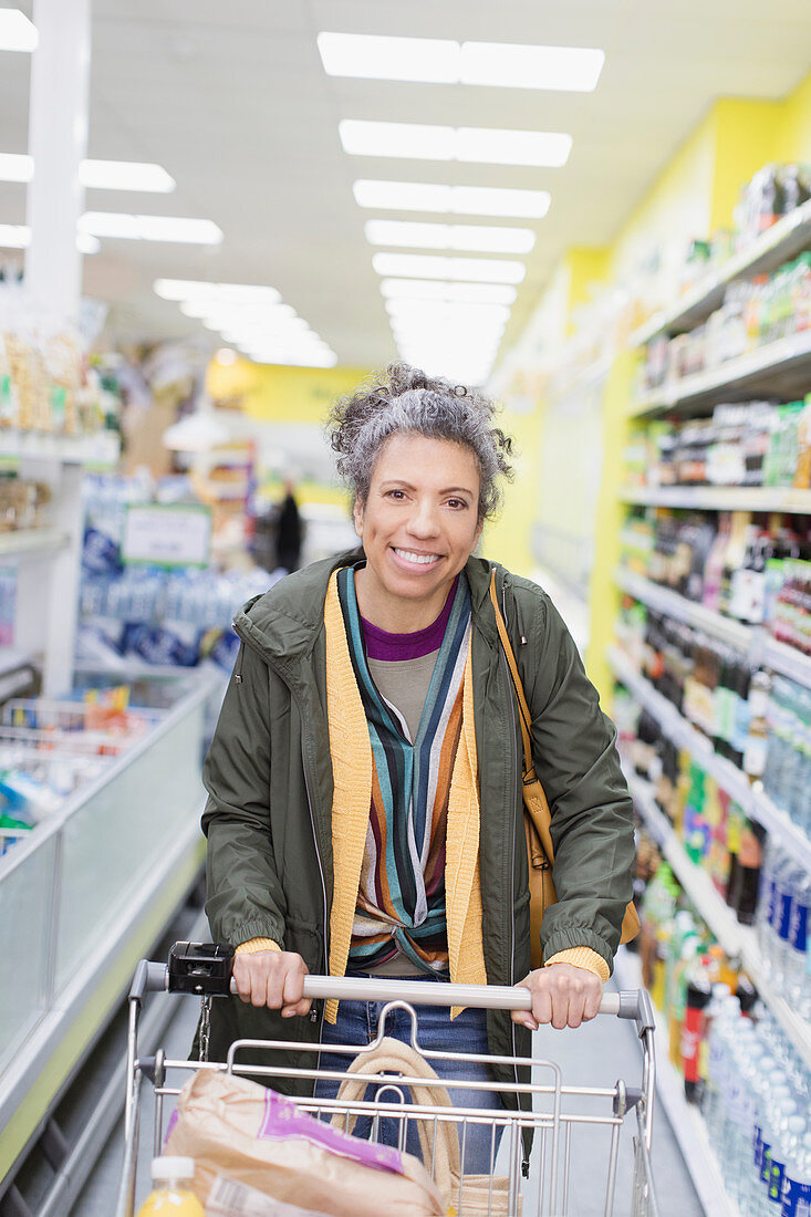 Woman pushing shopping cart in supermarket aisle