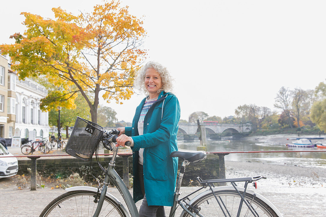 Portrait smiling senior woman bike riding along autumn river