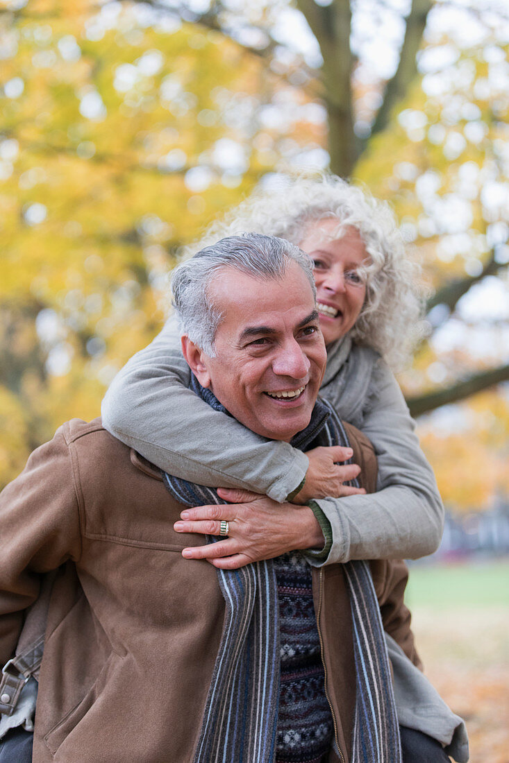 Playful, smiling senior couple piggybacking in autumn park