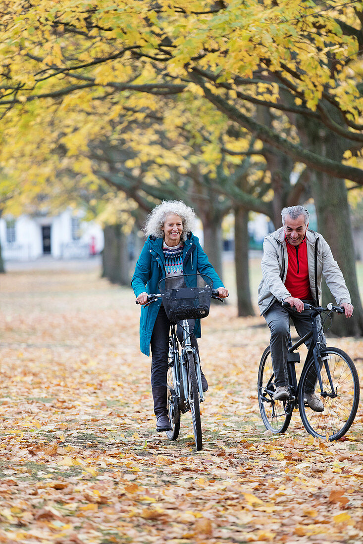 Senior couple bike riding among leaves in autumn park