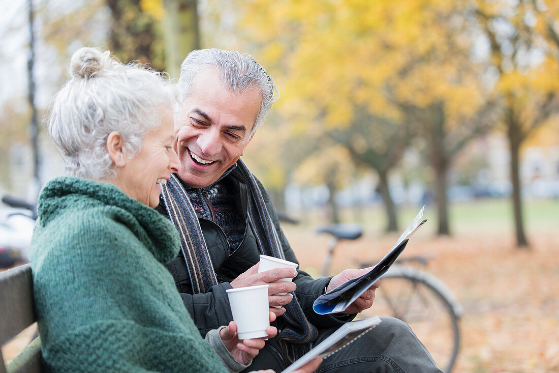 Couple reading newspaper and drinking coffee on bench