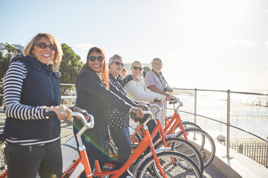Active senior tourist friends on bicycles on sunny boardwalk