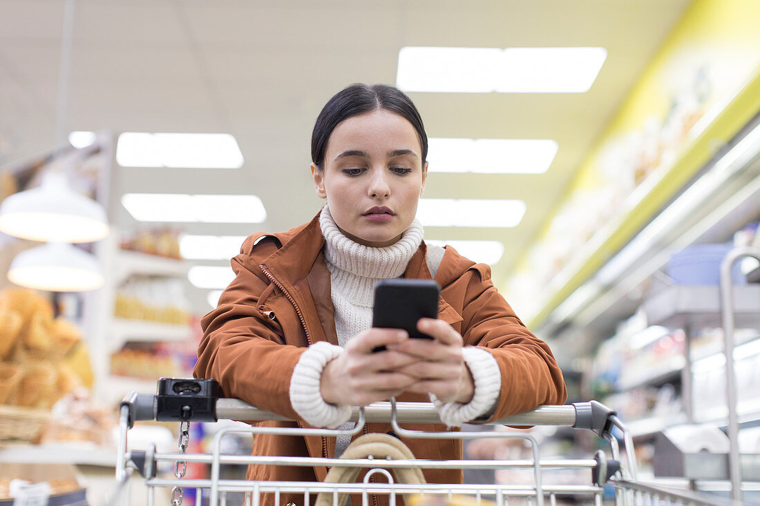 Young woman with smart phone shopping in grocery store