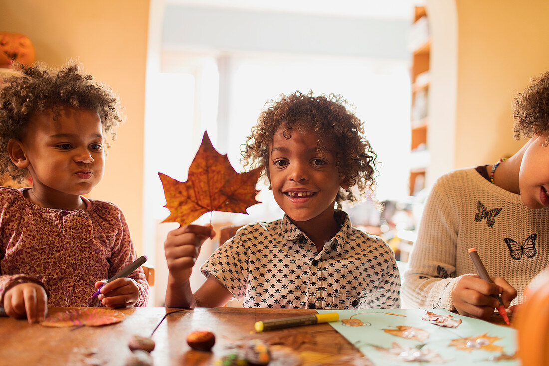 Boy with autumn leaf doing crafts with sisters at table