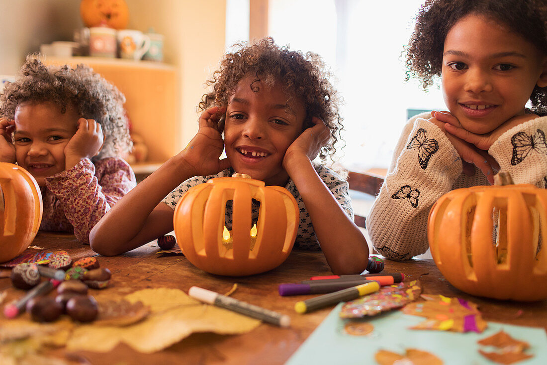 Portrait happy brother and sisters carving pumpkins at table