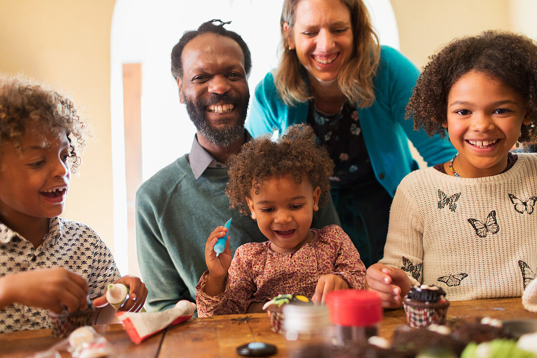 Happy multiethnic family decorating cupcakes at table