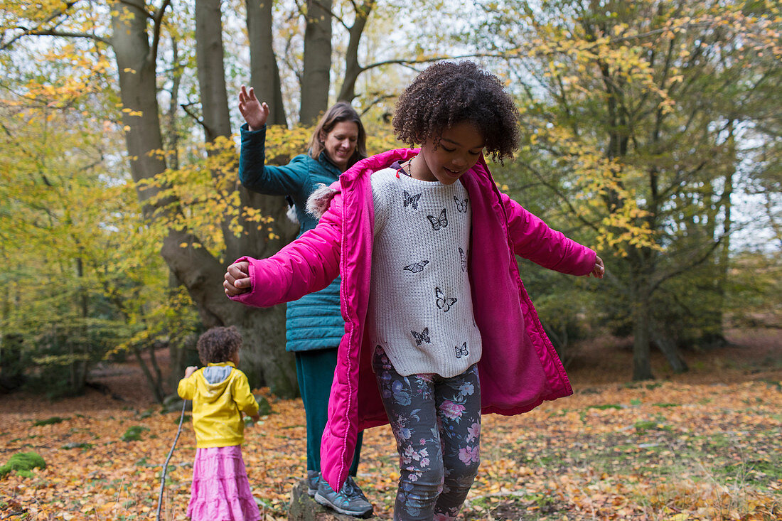 Mother and daughters balancing on fallen log in autumn woods