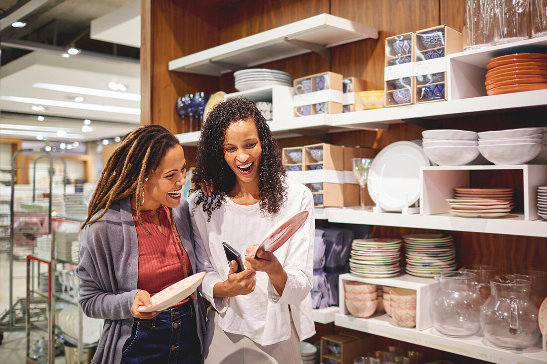 Happy women friends shopping for plates in home goods store