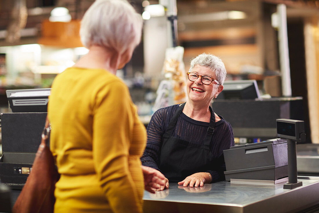 Senior female cashier greeting customer at supermarket