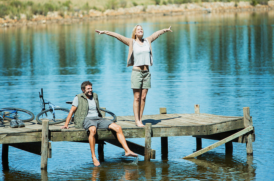 Exuberant woman with arms outstretched on dock over lake