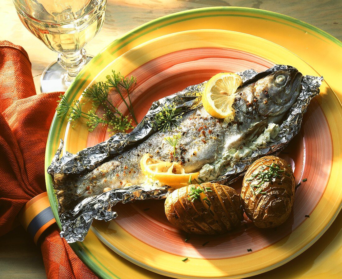 Trout, baked in foil, with baked potatoes on plate